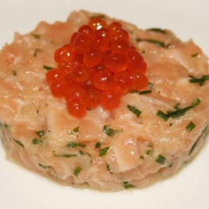 Un plat de Tartare de Saumon, généreusement garni de caviar rouge, est élégamment servi sur une assiette blanche immaculée.