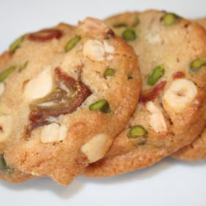 Trois biscuits sablés aux noix et morceaux verts reposent sur une surface blanche.