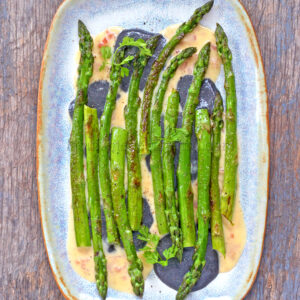 Asperges grillées à la perfection, servies sur une assiette bleue et arrosées d'une riche sauce au beurre blanc, garnie d'herbes fraîches.