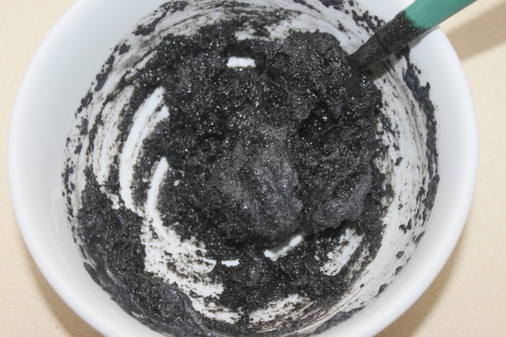 Un bol blanc contenant un mélange épais de tahiné noir noir avec un ustensile à manche vert.