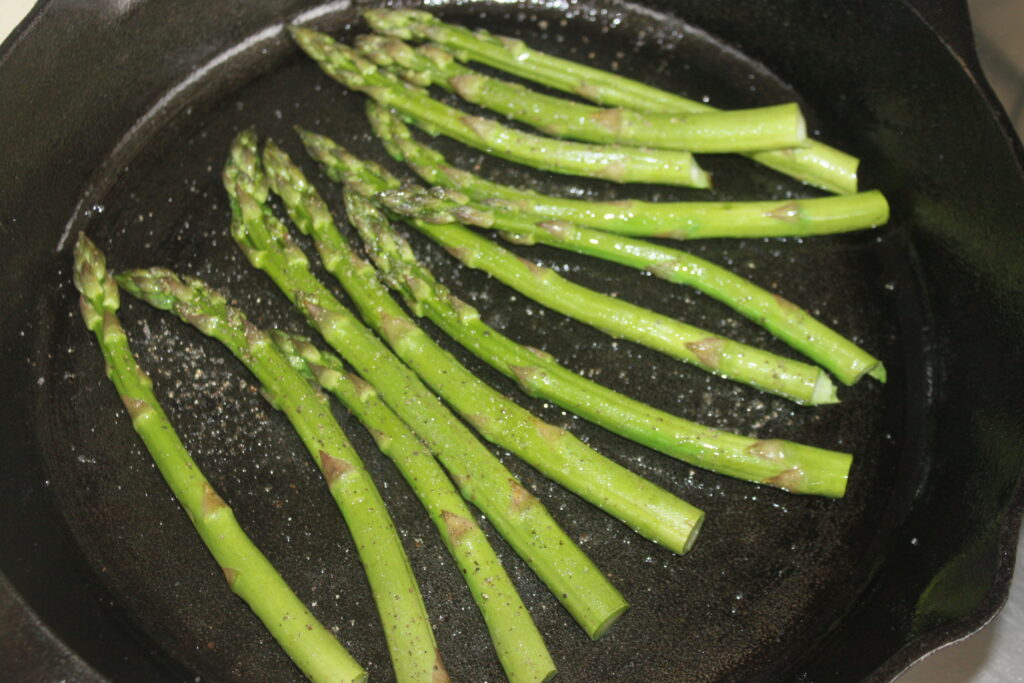 Les pointes d'asperges sont sautées avec de l'huile et des assaisonnements dans une poêle noire, prêtes à être servies avec un filet de tahiné noir.