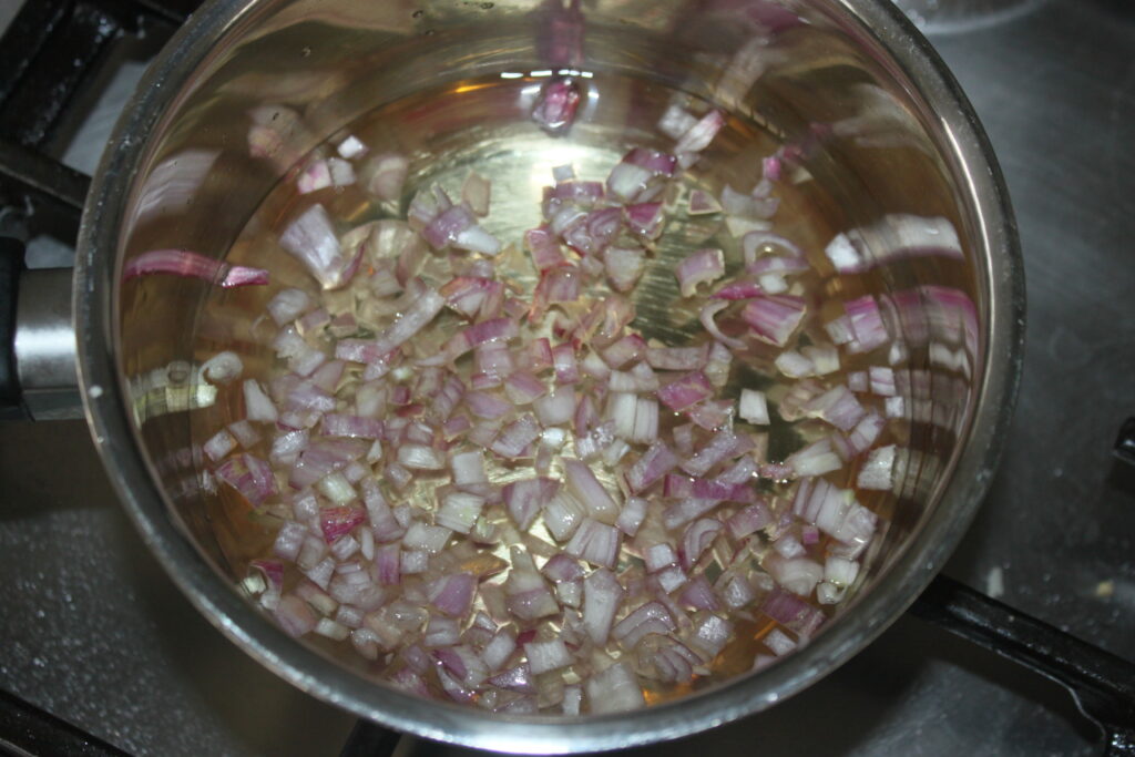 Les oignons rouges hachés mijotent dans une casserole en acier inoxydable avec du liquide sur la cuisinière, à côté d'un plat de beurre blanc.