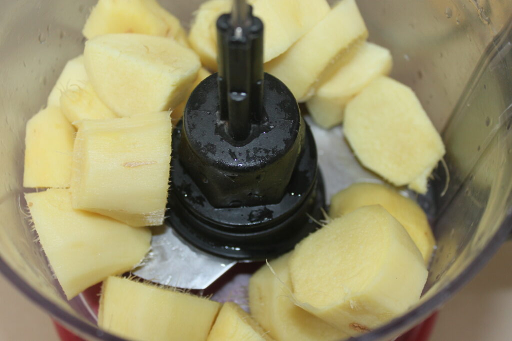 Morceaux de racine de gingembre coupés en cubes dans un bol de robot culinaire, prêts à être transformés pour créer une sauce fraîche et savoureuse.