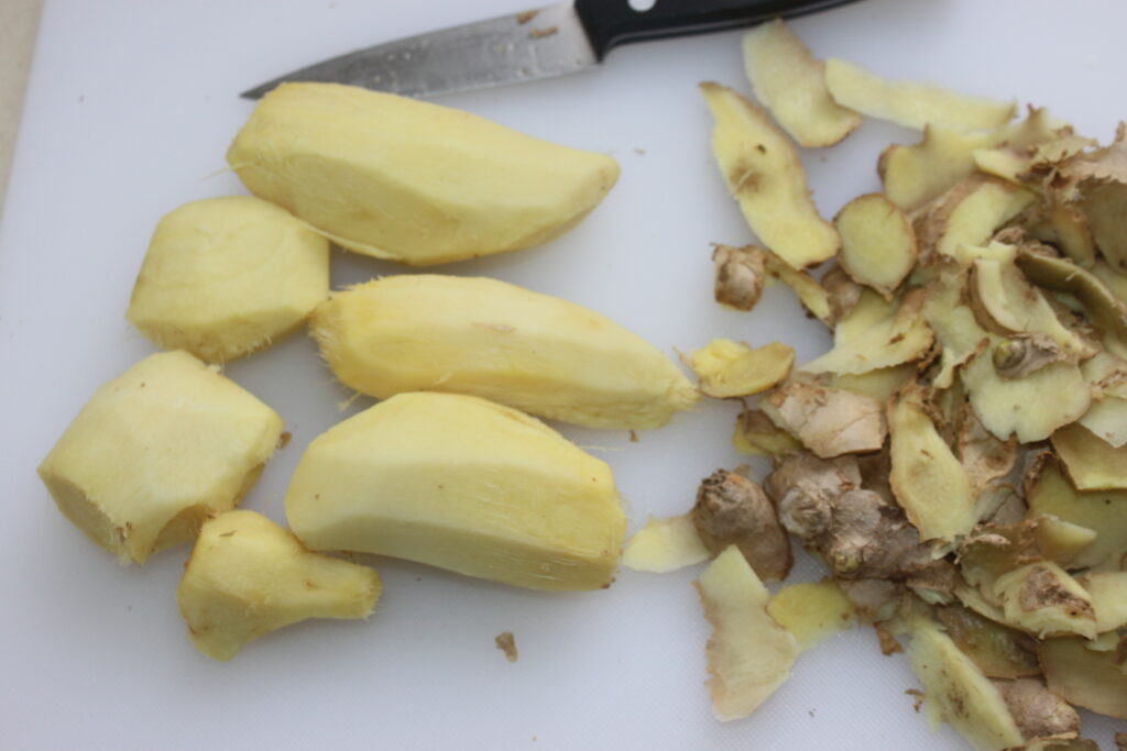 Les morceaux de gingembre pelés et les écorces de gingembre sont placés sur une planche à découper blanche à côté d'un petit couteau, parfait pour créer une sauce au gingembre frais.