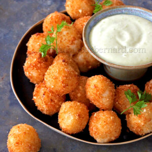 Une assiette de boules de Mozza dorées garnies de persil, servies avec un petit bol de trempette crémeuse à la mayonnaise au wasabi.