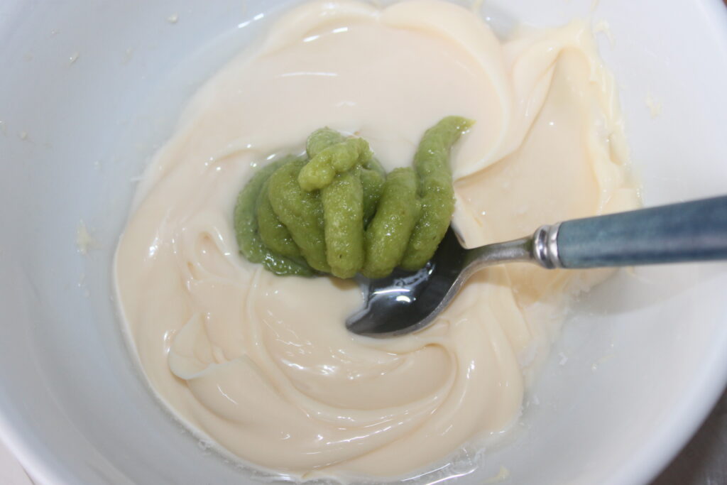 Un bol contenant un mélange de mayonnaise blanche et de wasabi vert, avec une cuillère nichée à l'intérieur.