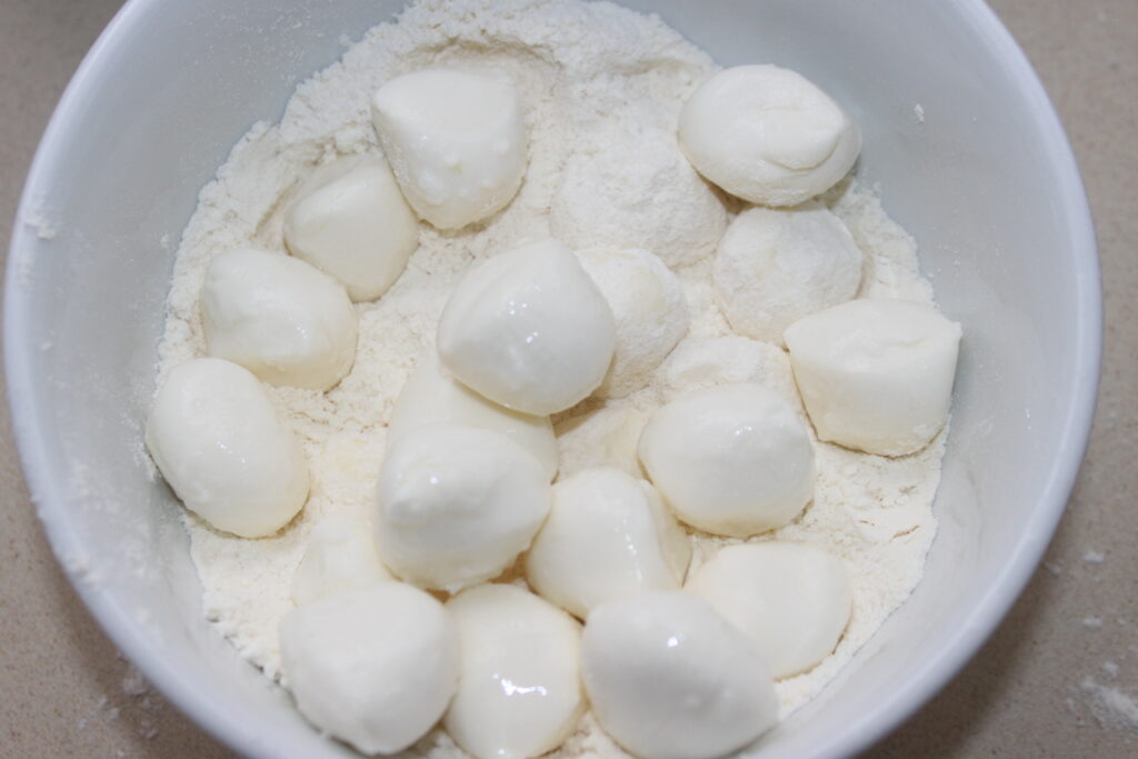 Un bol blanc contenant de petites boules rondes de Mozza posées sur un lit de farine, parfaites pour tremper dans de la mayonnaise au wasabi.