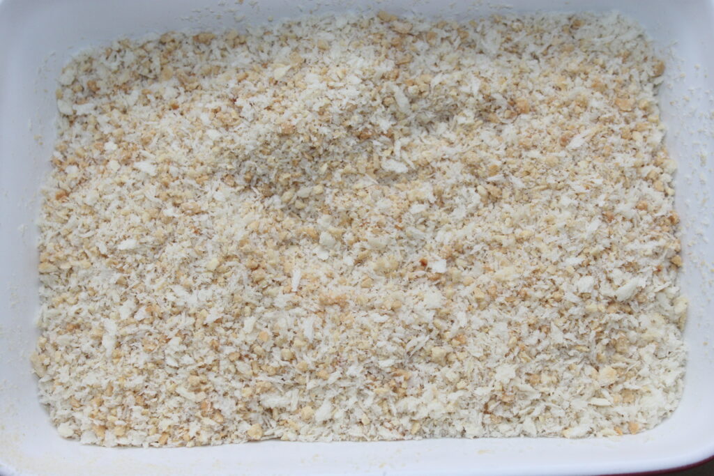 Gros plan d'un récipient rectangulaire blanc rempli de chapelure finement moulue, parfait pour enrober de délicieuses boules de Mozza.