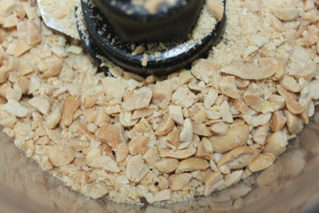 Image en gros plan de cacahuètes hachées dans un robot culinaire, avec un soupçon de wasabi ajoutant une touche unique.