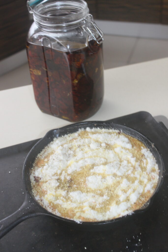 Une poêle en fonte contenant un plat cuit au four garni de sucre se trouve à côté d'un bocal en verre rempli de haricots blancs et de tomates séchées sur un comptoir de cuisine.