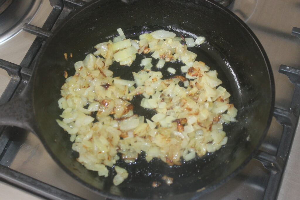 Des oignons hachés sont sautés dans l'huile avec des haricots blancs dans une poêle noire sur une cuisinière.