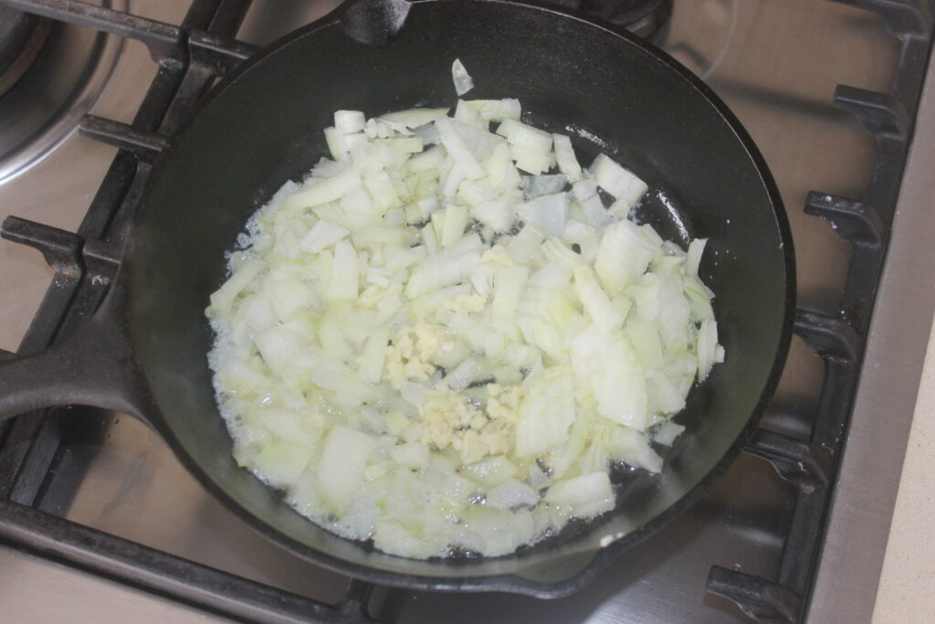 Des oignons hachés, de l'ail émincé et des haricots blancs sont sautés dans une poêle noire sur une cuisinière.