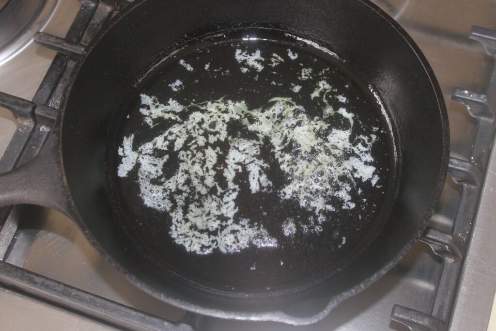 Une poêle en fonte avec du beurre fondu chauffé sur un brûleur de cuisinière, prête pour les haricots blancs.