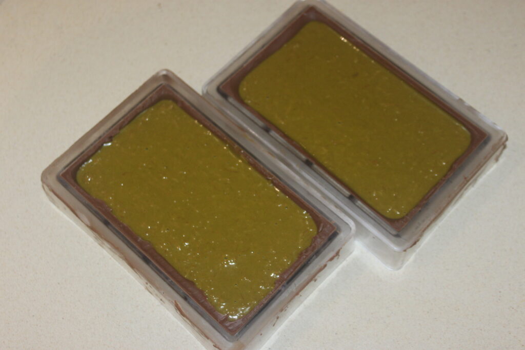 Deux moules rectangulaires remplis d'un mélange brun verdâtre, posés sur une surface de couleur claire, parfaits pour créer votre propre Chocolat de Dubaï et découvrir le riche goût du chocolat de Dubaï à la maison.