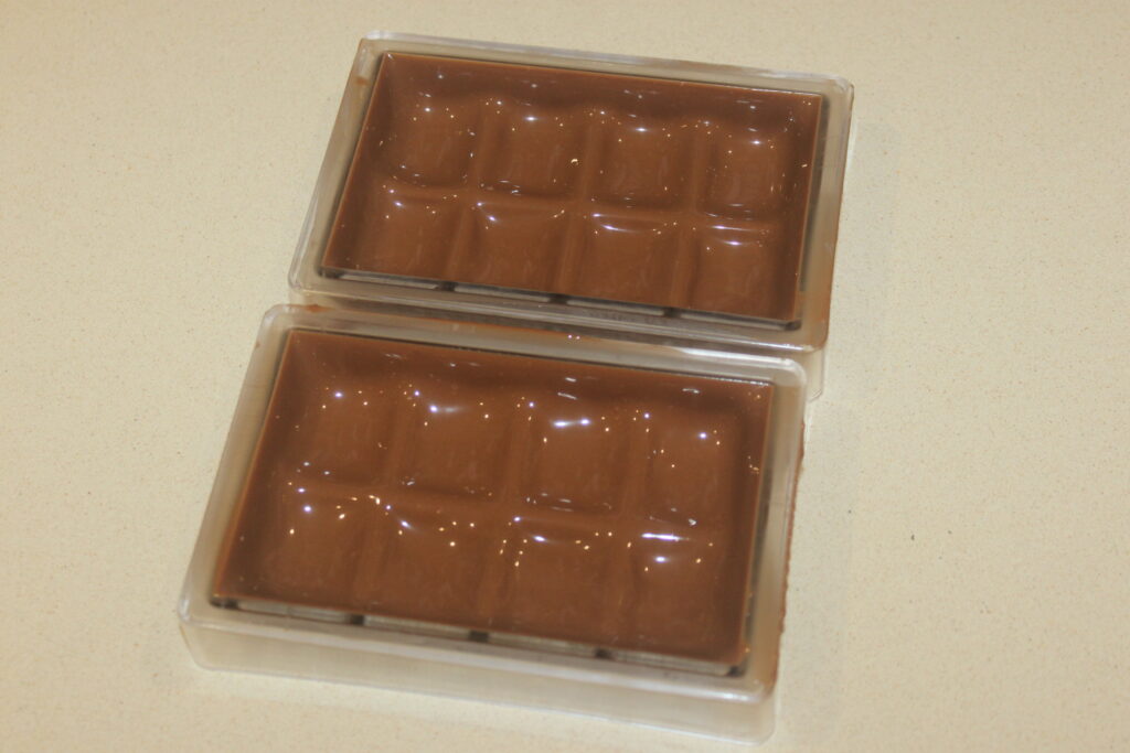 Deux moules à barres de chocolat en plastique remplis de chocolat de Dubaï fondu sont placés sur un comptoir de couleur claire, capturant l'essence de la fabrication de chocolat de luxe.