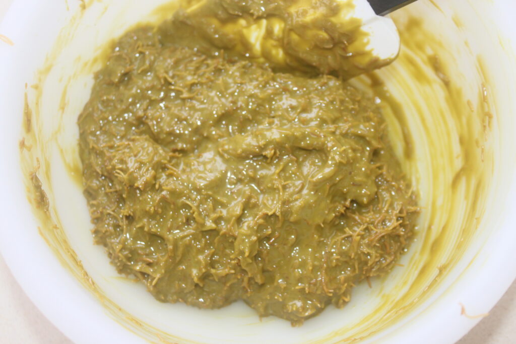 Un bol blanc contenant une pâte épaisse, brun verdâtre, rappelant le chocolat de Dubaï, mélangée à l'aide d'une spatule.