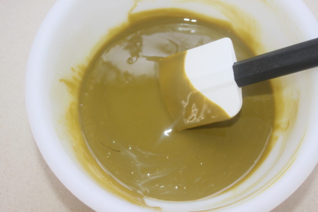 Un bol blanc avec une spatule blanche contenant un mélange épais, brun verdâtre, inspiré des riches saveurs du chocolat de Dubaï.