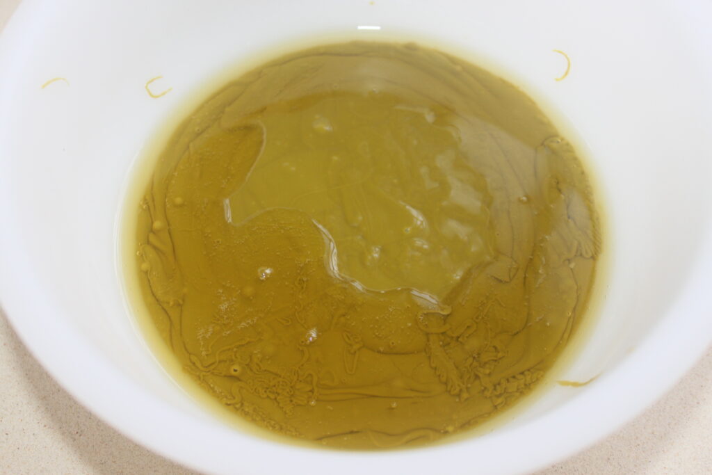 Un bol blanc rempli d'huile d'olive, sa surface lisse vert doré scintillant de petites bulles et de stries une élégance rappelant le chocolat de luxe de Chocolat de Dubaï.