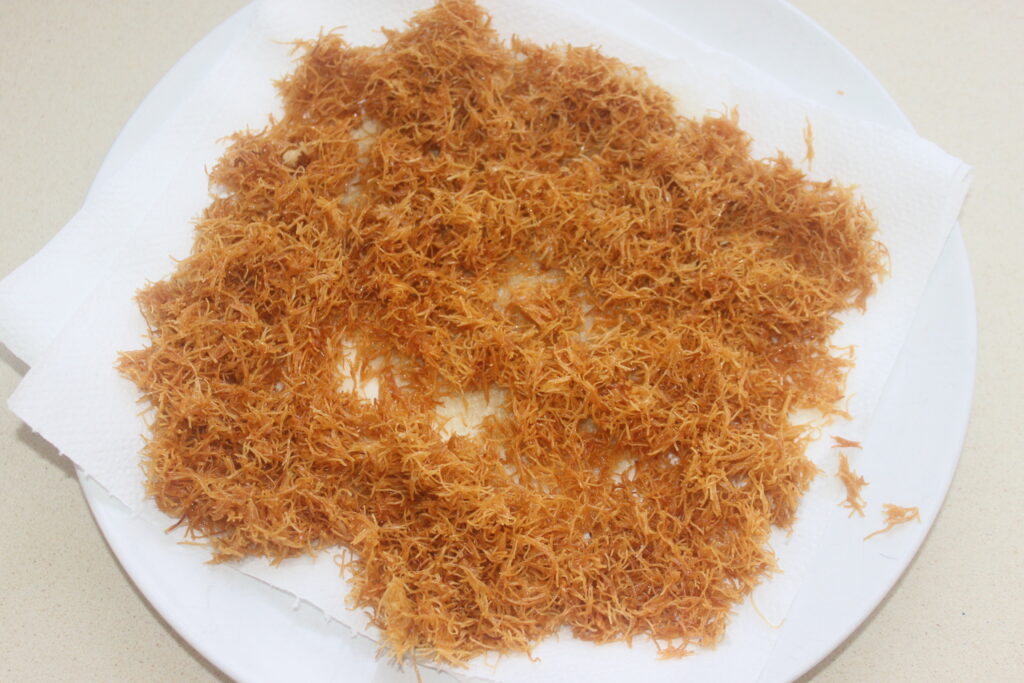 Une pâte râpée dorée et croustillante est posée sur une serviette en papier blanche au sommet d'une assiette blanche, invitante et fraîche, prête à être dégustée, peut être parfaitement associée au chocolat de luxe de Chocolat de Dubaï.