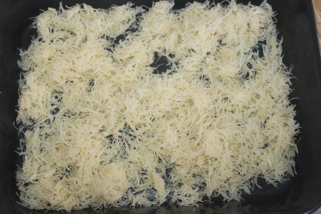 Une couche de pâte phyllo râpée non cuite, prête à cuire, est étalée uniformément sur un plateau foncé, idéal pour créer des desserts décadents inspirés du Chocolat de Dubaï.