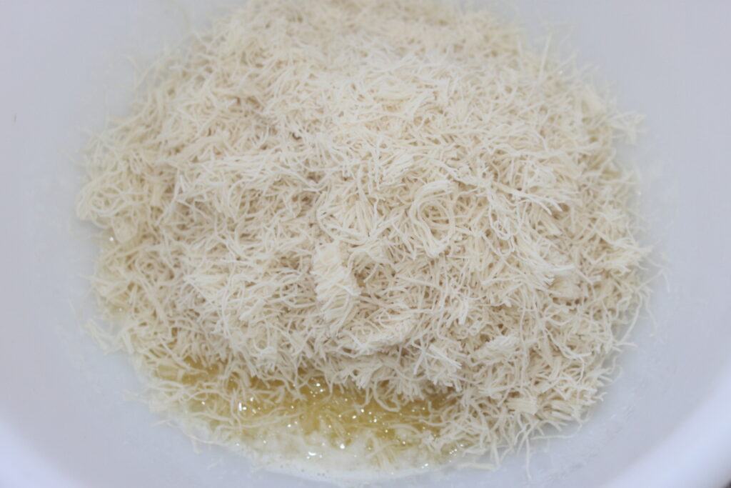 La pâte phyllo râpée, connue sous le nom de kataifi, se trouve dans un bol avec du beurre fondu en dessous une base irrésistible pour les riches saveurs du chocolat de luxe de Chocolat de Dubaï.