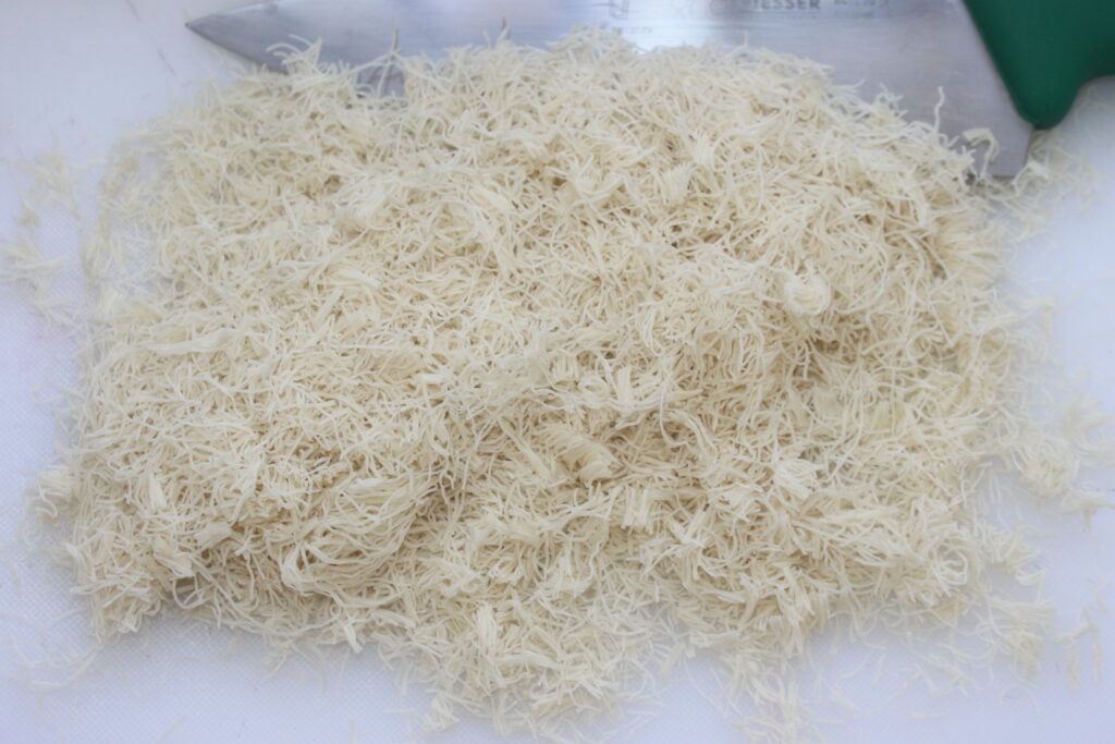 Un tas de légumes racines blancs râpés ou finement hachés est posé sur une surface blanche, avec un grand couteau de cuisine en arrière plan, rappelant la précision trouvée dans la fabrication du chocolat fin de Dubaï.