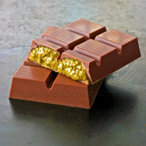 Une barre de chocolat de luxe est cassée en deux, révélant une garniture jaune crémeuse et texturée à l'intérieur un délice gourmand inspiré des saveurs du Chocolat de Dubaï.
