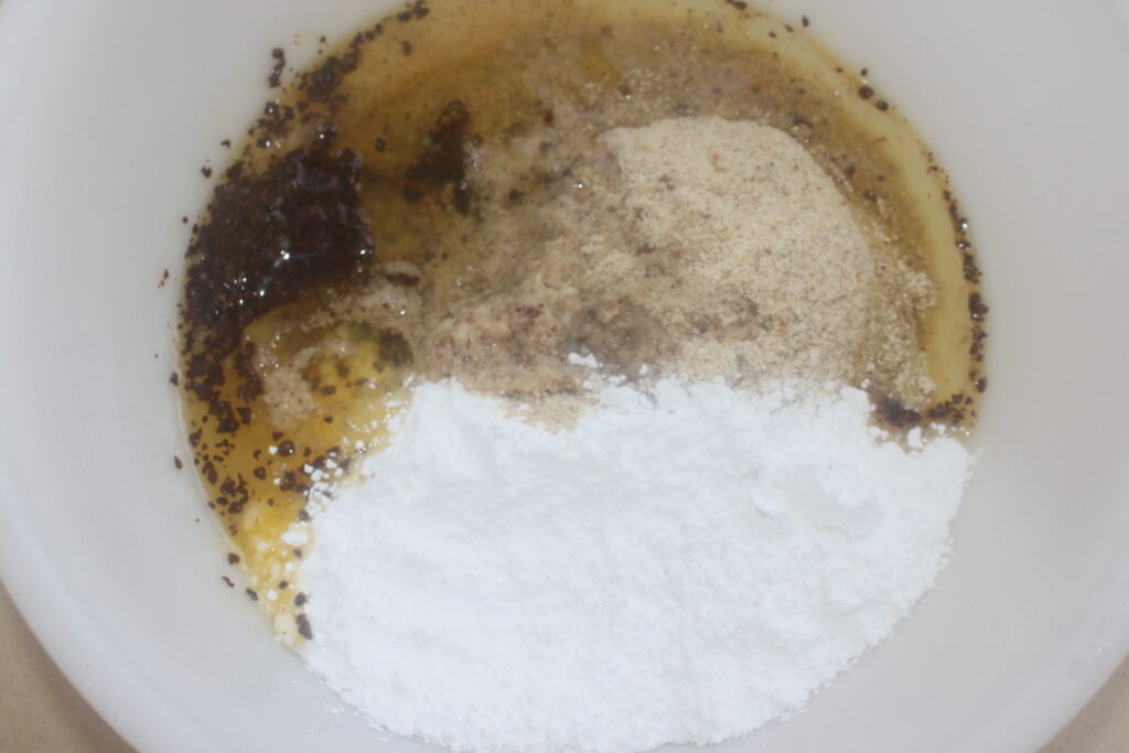 Un bol à mélanger contenant de la cassonade, de la farine d'amande, du sucre en poudre et des graines est prêt à se transformer en une délicieuse noisette financière, son arôme de noisette rappelant un café chaleureux.