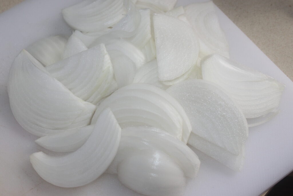 Des oignons blancs émincés préparent la scène sur une planche à découper impeccable, prêts à ajouter du piquant à une salsa piquante ou peut être à accompagner la copieuse bouchée de pâtes Bigoli.