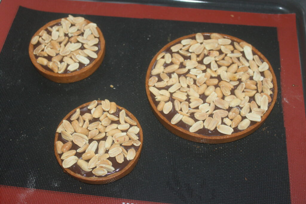 Trois exquises tartes au chocolat couronnées de cacahuètes reposent élégamment sur un tapis de cuisson.