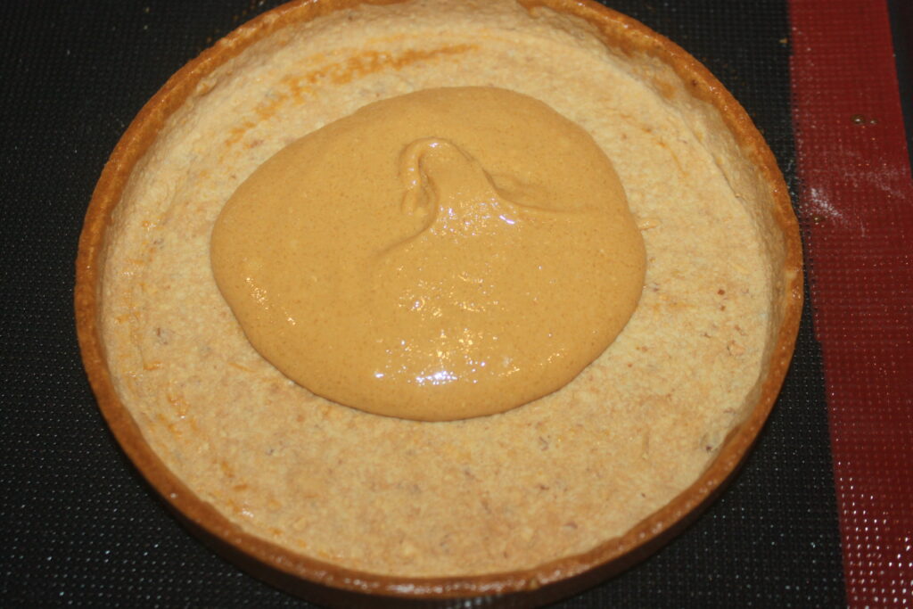 Croûte de tarte non cuite avec une couche de garniture épaisse de couleur caramel en son centre, accentuée par du chocolat riche et des cacahuètes croquantes.