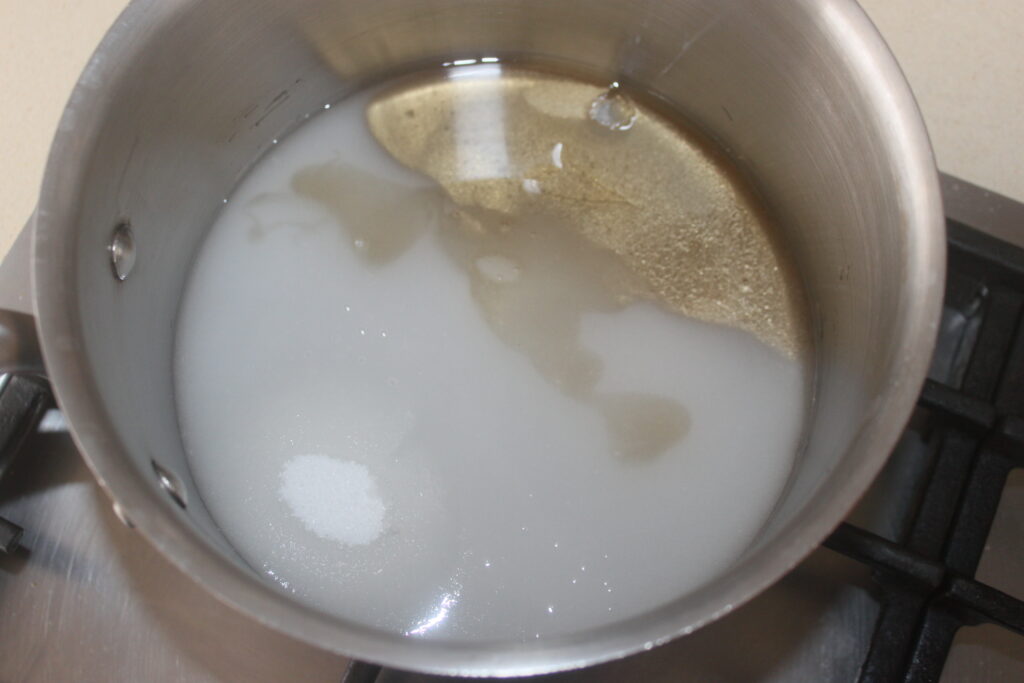 Une casserole en acier inoxydable sur une cuisinière contient de l'eau trouble et des cristaux de sucre, partiellement dissous, créant le début d'une base de tarte sucrée.