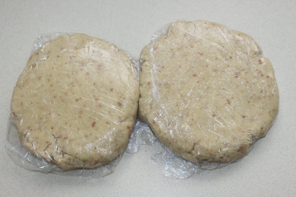 Deux disques de pâte à biscuits, parfaits pour une tarte au chocolat, sont emballés dans une pellicule plastique sur un comptoir de couleur claire.