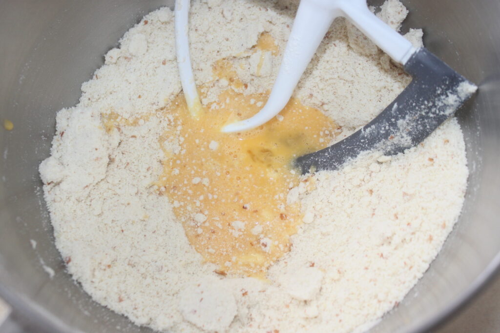 Un bol à mélanger avec de la farine, de la poudre d'amandes et des œufs battus combinés avec une palette de mixage pour une riche tarte au chocolat.