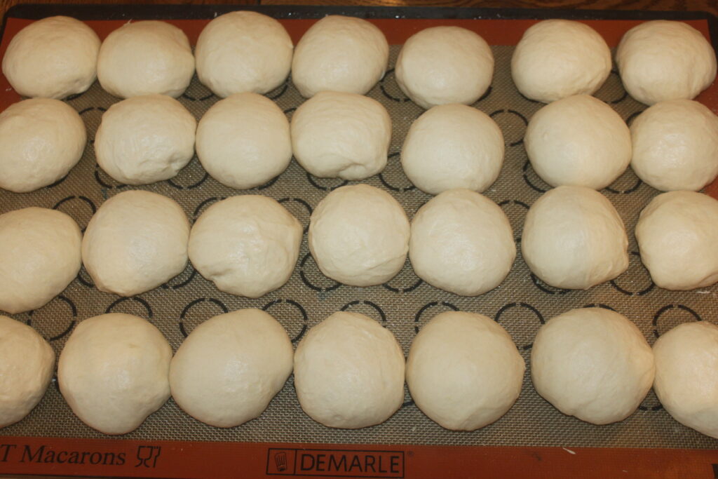 Rangées de petits pains moelleux crus disposés sur un tapis de cuisson antiadhésif.