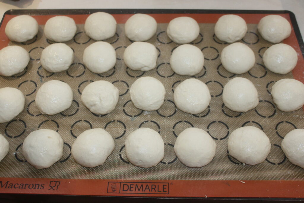 Des rangées de petits pains moelleux non cuits sont soigneusement disposées sur un tapis de cuisson en silicone, promettant une douceur moelleuse à chaque bouchée.