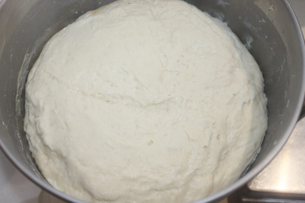 La boule de pâte moelleuse repose dans un bol en métal et monte progressivement jusqu'à se transformer en petits pains moelleux et aérés.