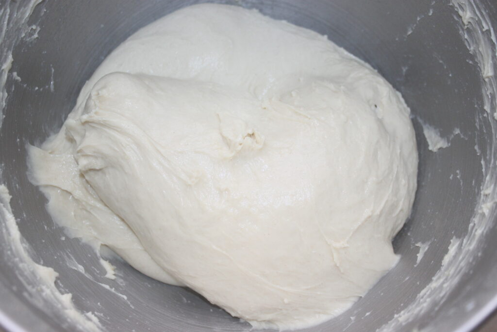 Vue rapprochée d'une pâte blanche et lisse dans un bol à mélanger en métal, prête à être façonnée en petits pains moelleux.