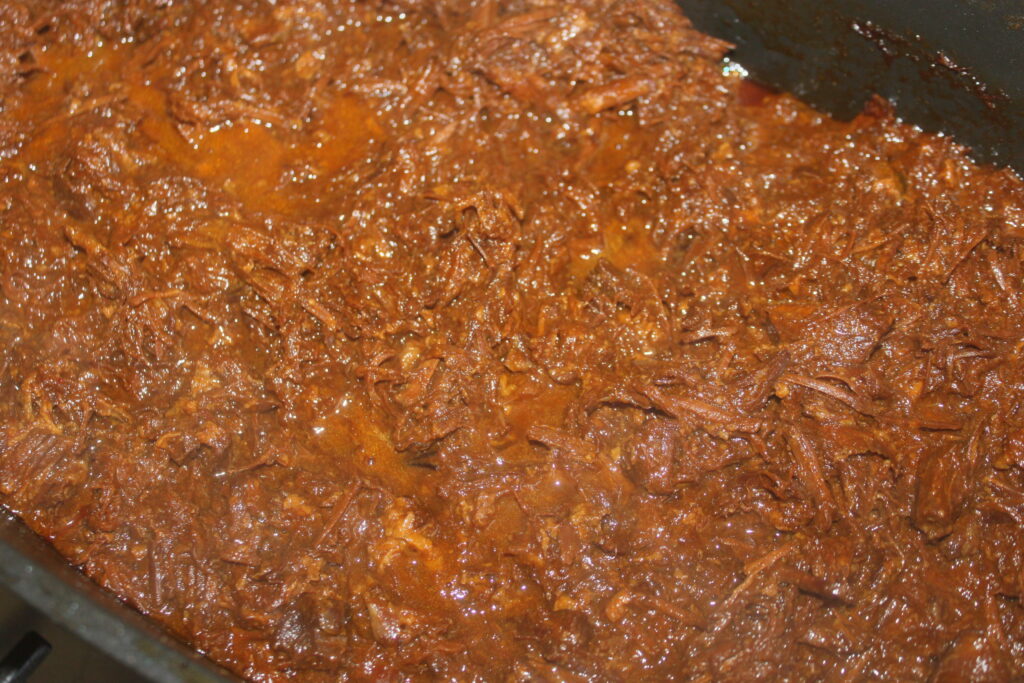 Gros plan de bœuf effiloché dans une riche sauce brune, assaisonné et cuit dans une casserole.