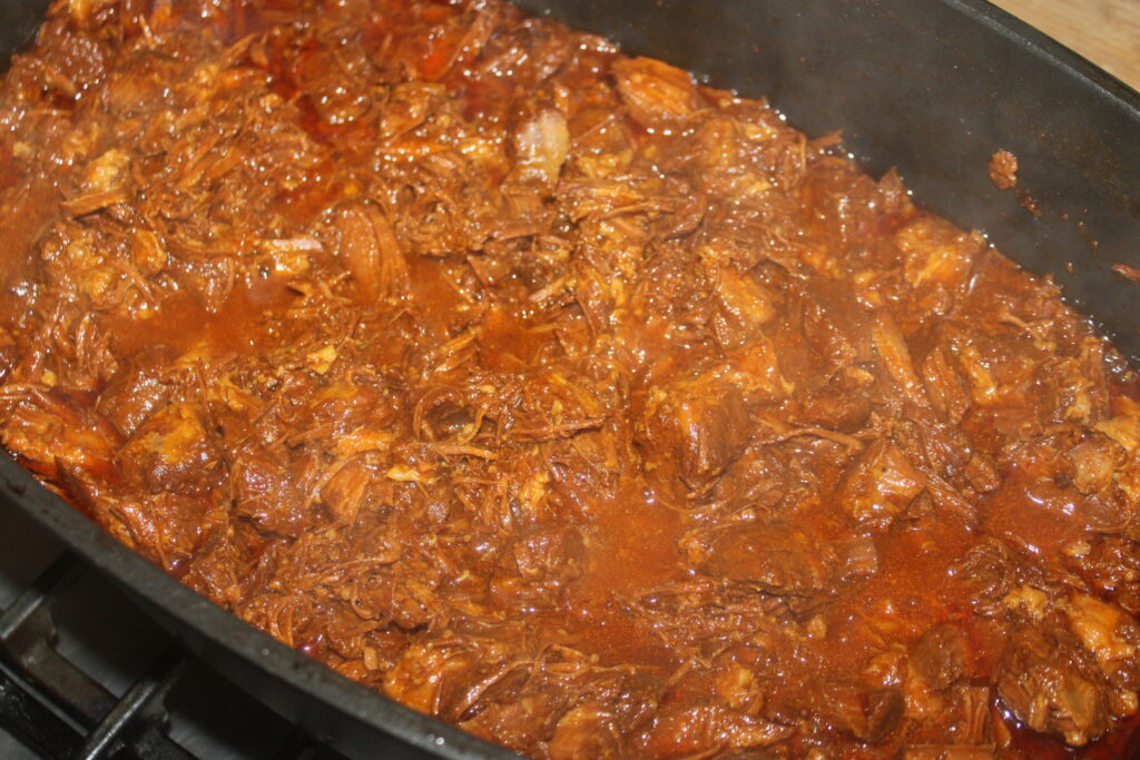 Viande effilochée dans une riche sauce rouge en train de cuire dans une grande poêle.