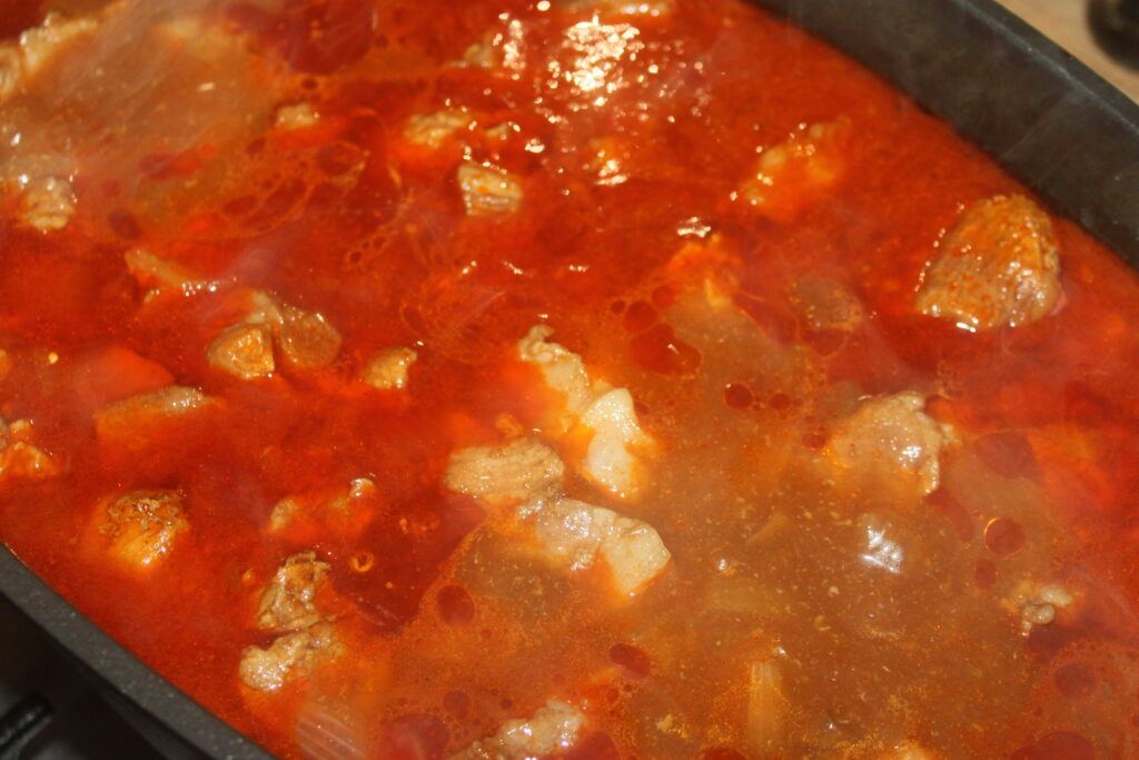 Un pot de ragoût avec des morceaux de viande mijotant dans un bouillon riche et rouge.