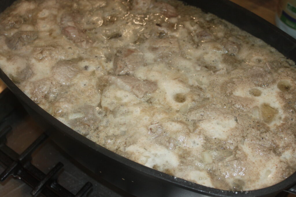 Gros plan d'une casserole mijotant avec des morceaux de viande dans un liquide mousseux et bouillonnant sur une cuisinière.