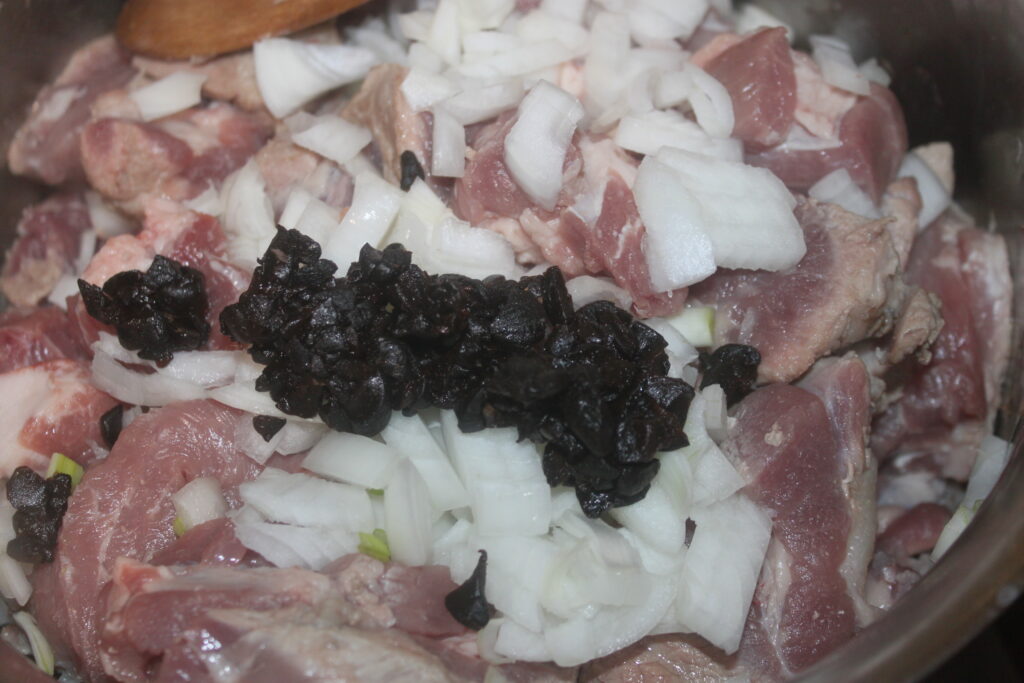 Viande crue hachée avec des oignons coupés en dés et des olives noires dans un bol.