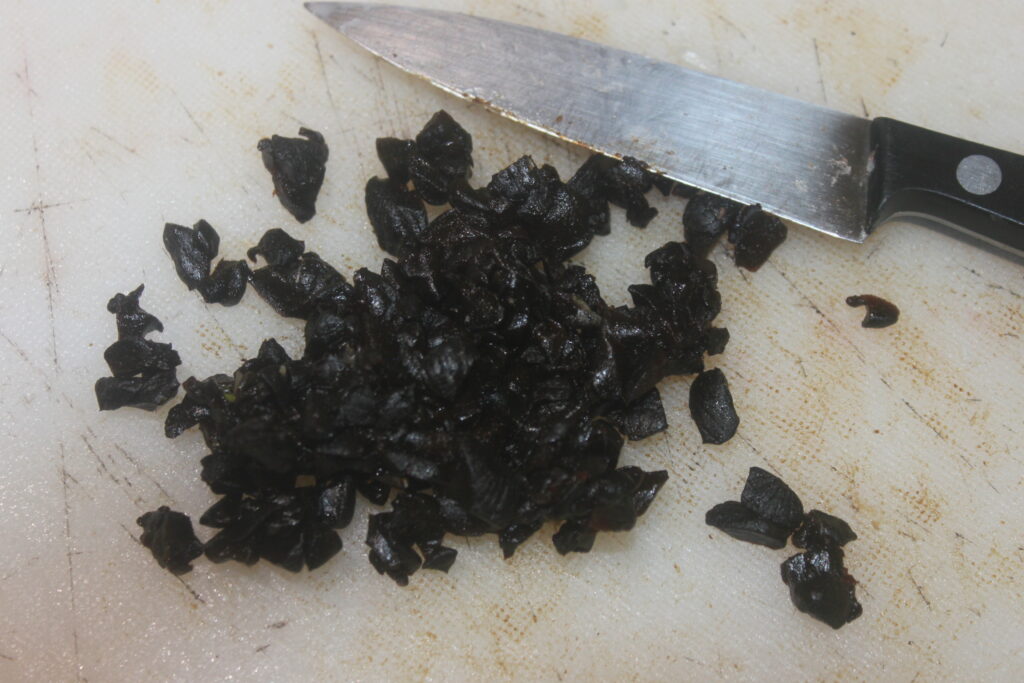 Ail noir haché sur une planche à découper à côté d'un couteau.