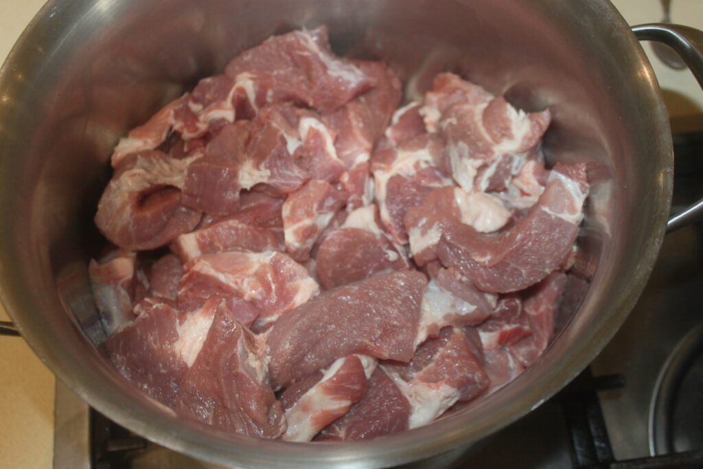 Morceaux de viande crue dans une grande casserole en acier inoxydable sur une cuisinière.