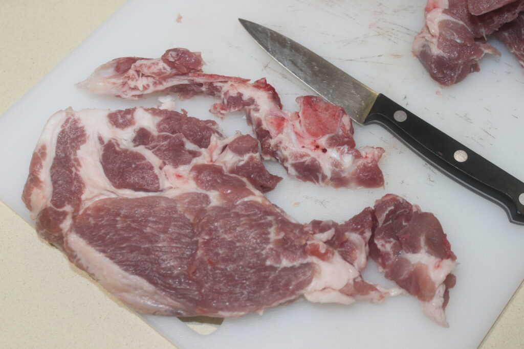 Morceaux de viande crue sur une planche à découper avec un couteau à côté.