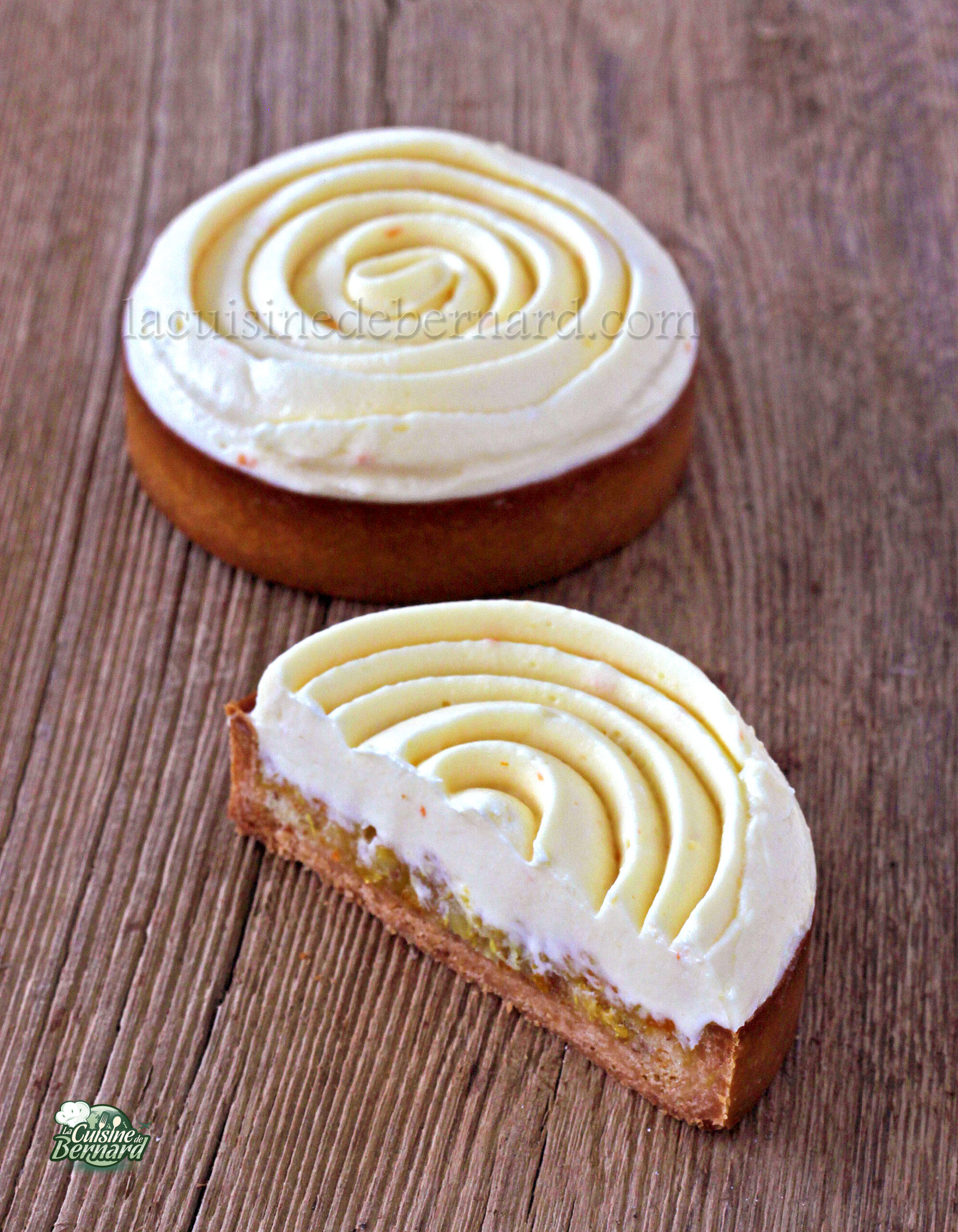 Une tarte et une pâtisserie sont posées sur une surface en bois, chacune ornée d'un glaçage blanc en spirale ; la tarte est coupée en deux pour révéler un intérieur crémeux et succulent.