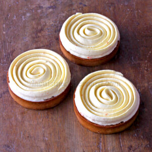 Trois pâtisseries rondes recouvertes d'un glaçage à la crème en spirale reposent sur une surface en bois.