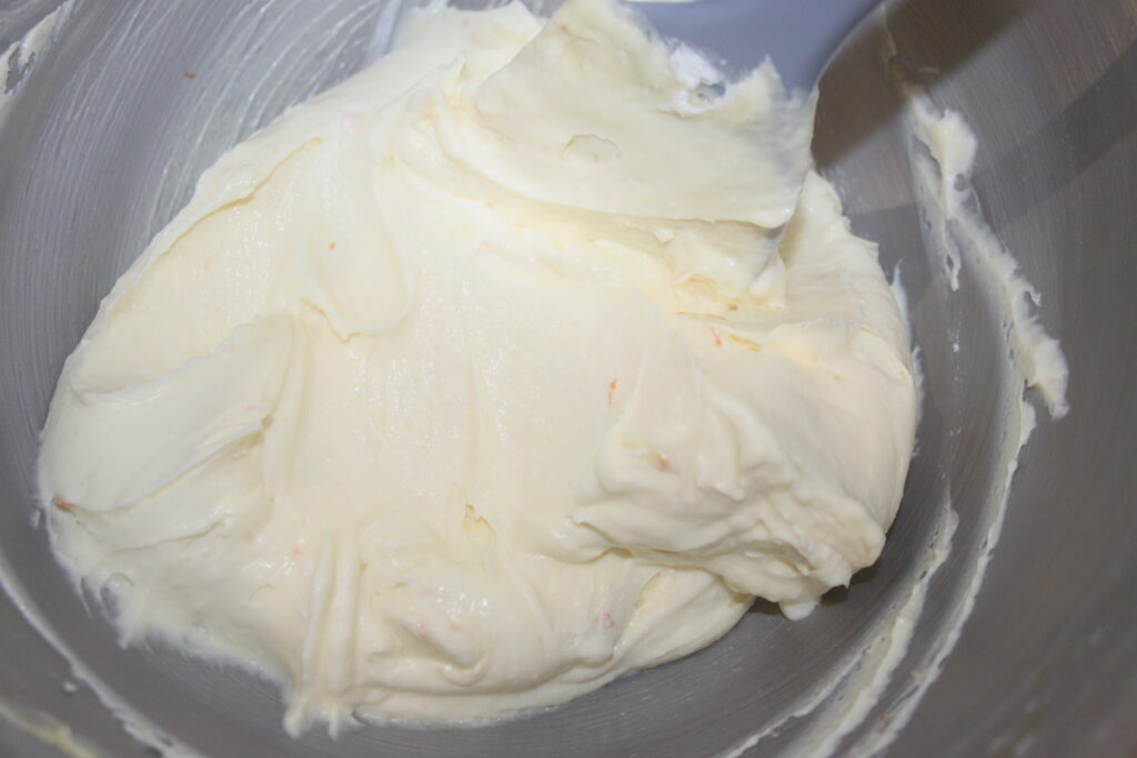 Un bol en métal rempli de beurre crémeux et lisse est mélangé avec une spatule, prêt à réaliser de délicieuses tartelettes à la crème d'orange.