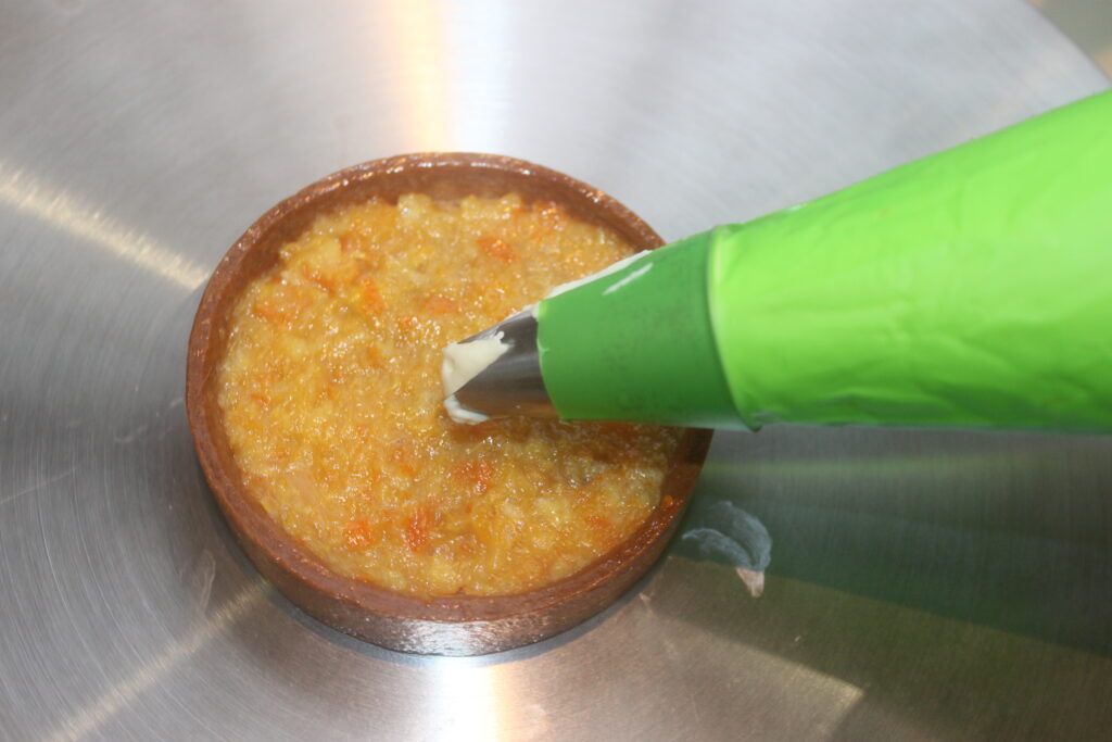 Une poche à douille verte applique élégamment le glaçage sur des Tartelettes crème d'orange sur une surface métallique.